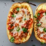 One half of a stuffed spaghetti squash topped with melted cheese and chopped parsley.