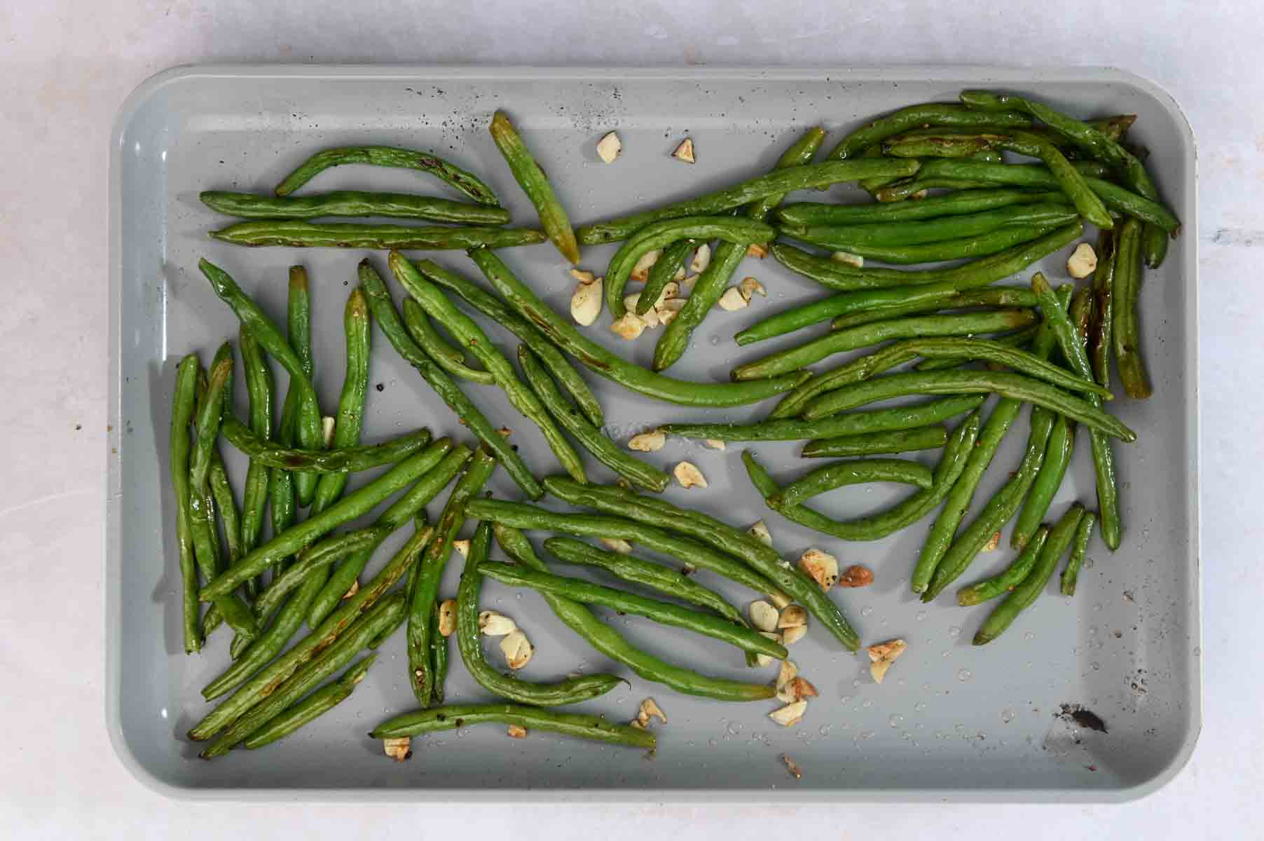 Roasted green beans and garlic on a sheet pan.