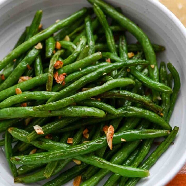 Roasted green beans in a bowl with golden garlic.