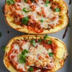 Two halves of a stuffed spaghetti squash topped with melted cheese and chopped parsley.