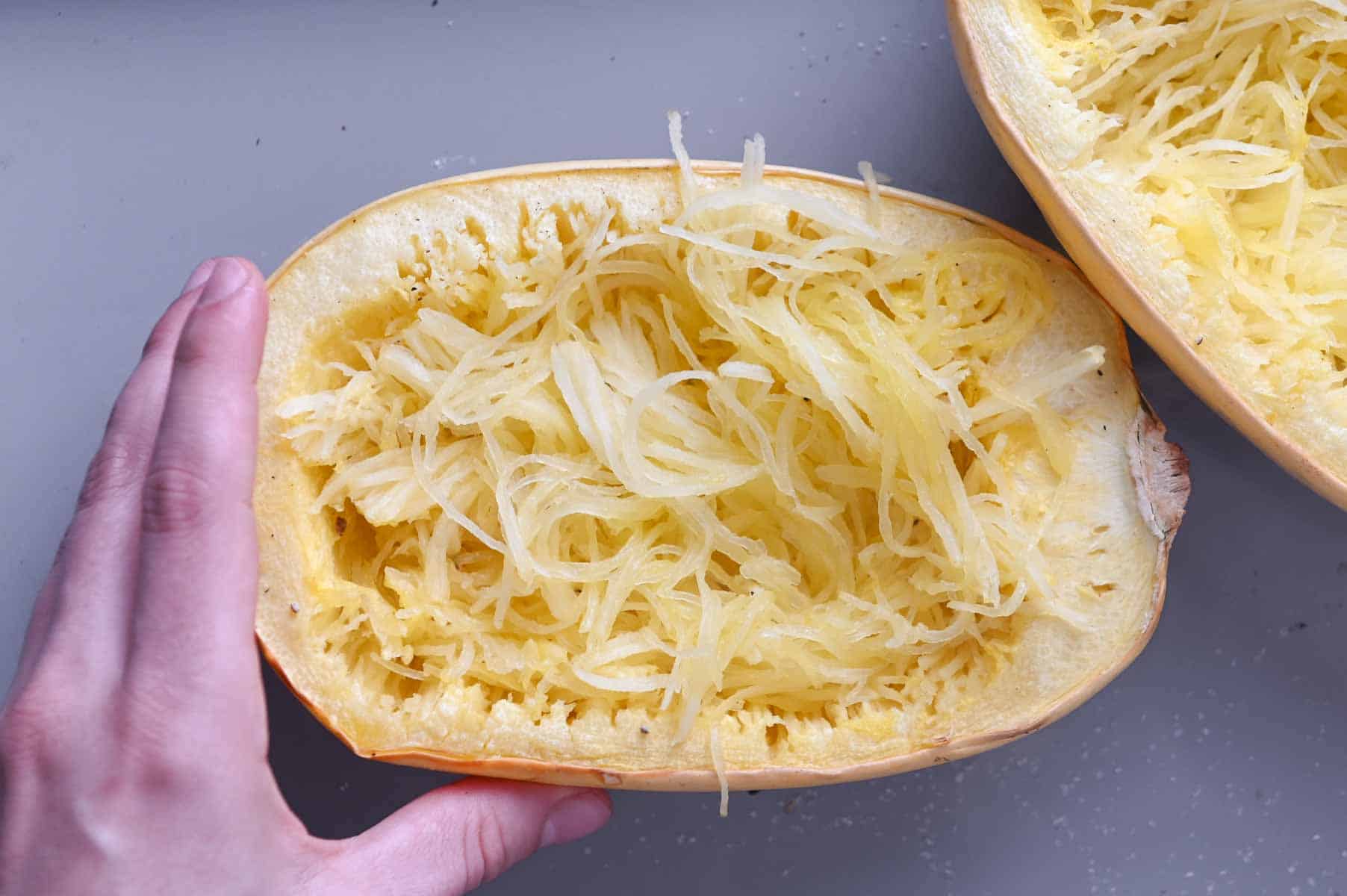 Hand grasping half of a spaghetti squash showing the shreds of squash.