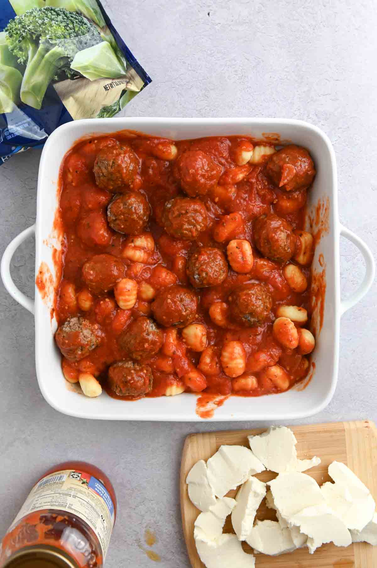 Meatballs, pasta sauce, and gnocchi in a white square baking dish.