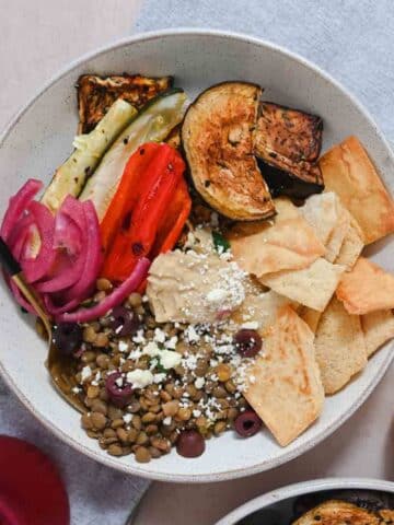 Bowl filled with hummus, roasted vegetables, and a variety of toppings.