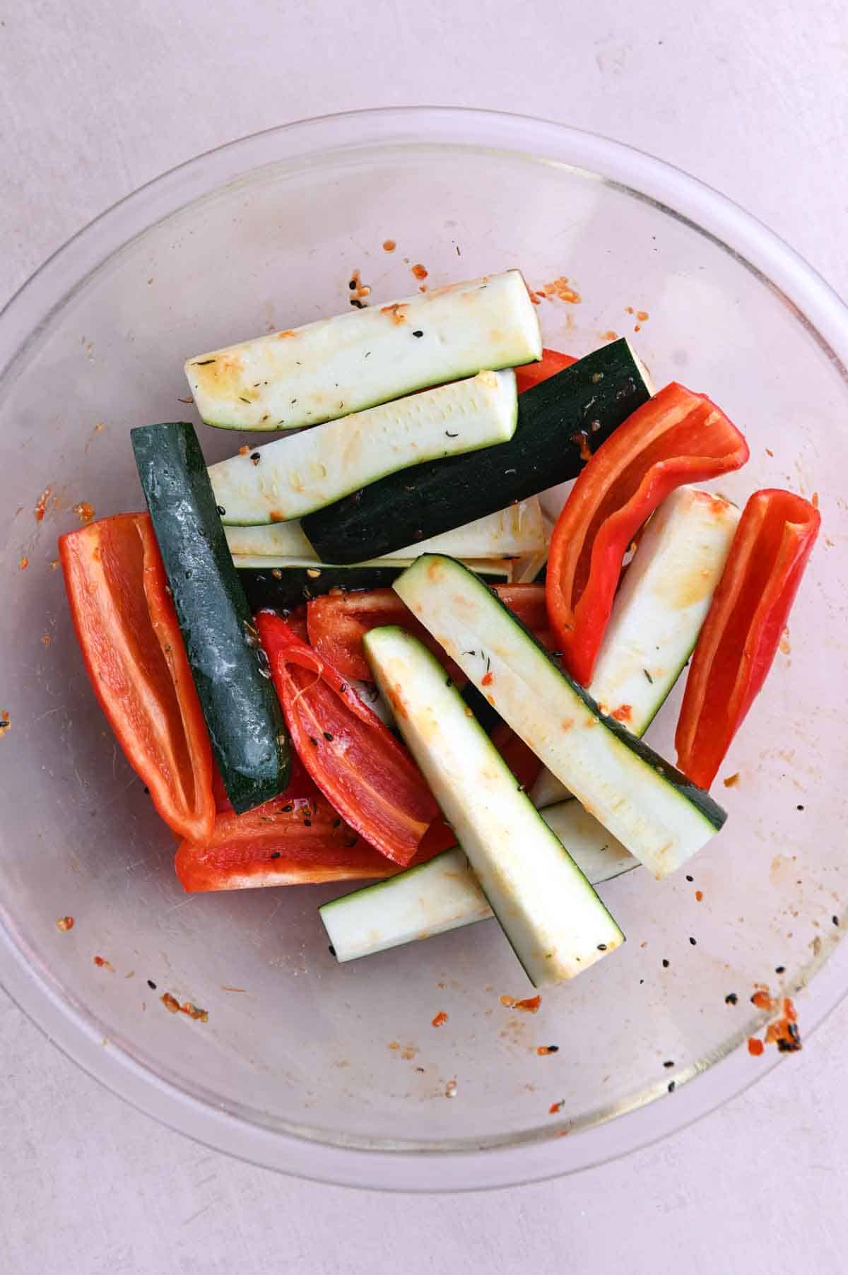 Zucchini wedges and red bell pepper strips in a large glass bowl.
