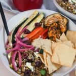 Bowl filled with hummus, roasted vegetables, and a variety of toppings.