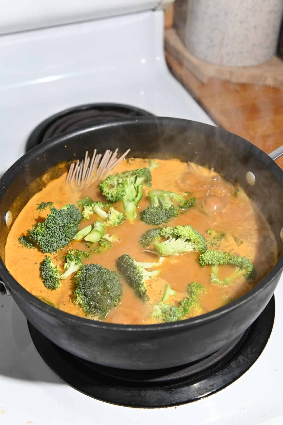 Noodles and fresh broccoli florets boiling in red broth.