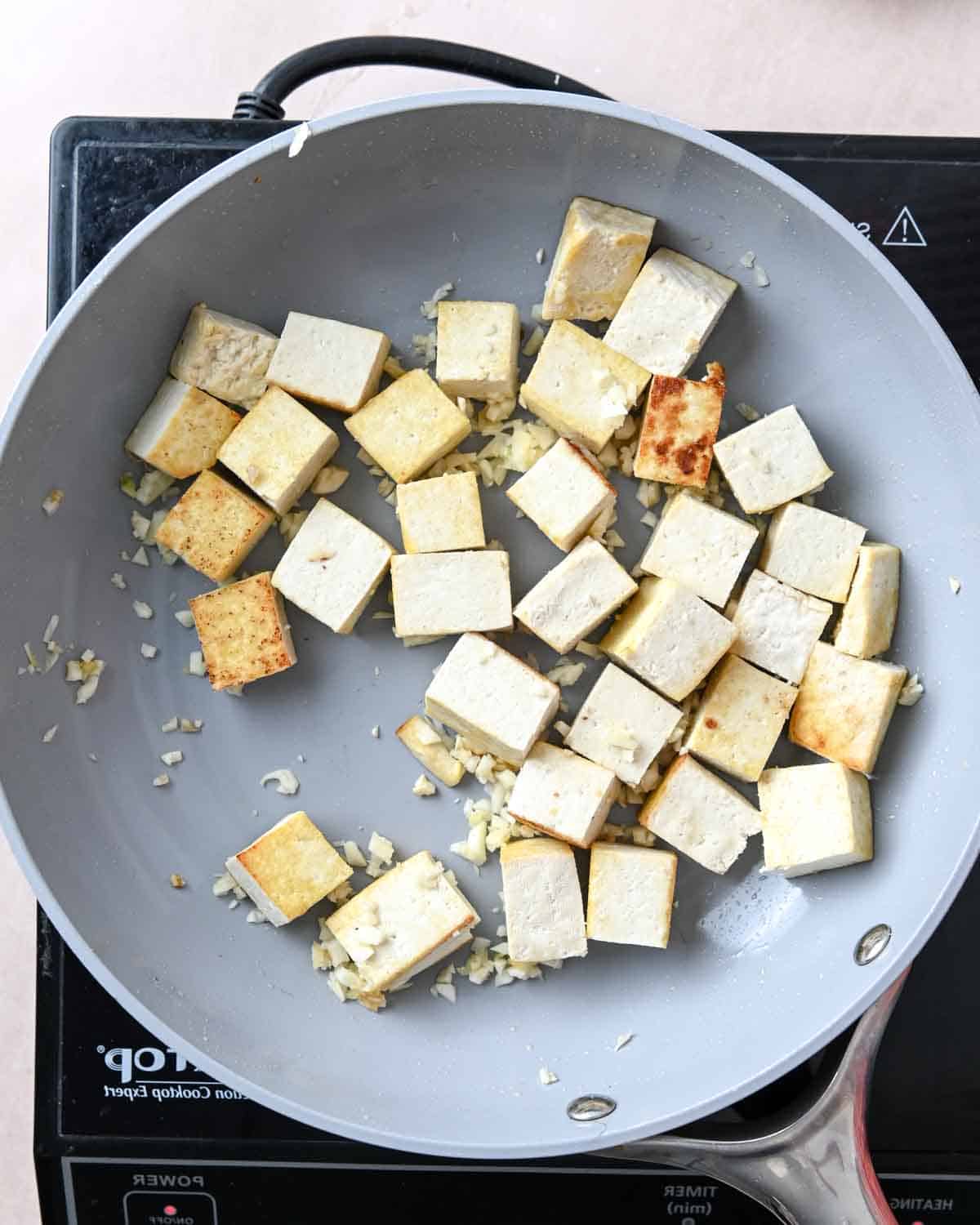 Lightly browned cubed tofu and minced garlic in a skillet.