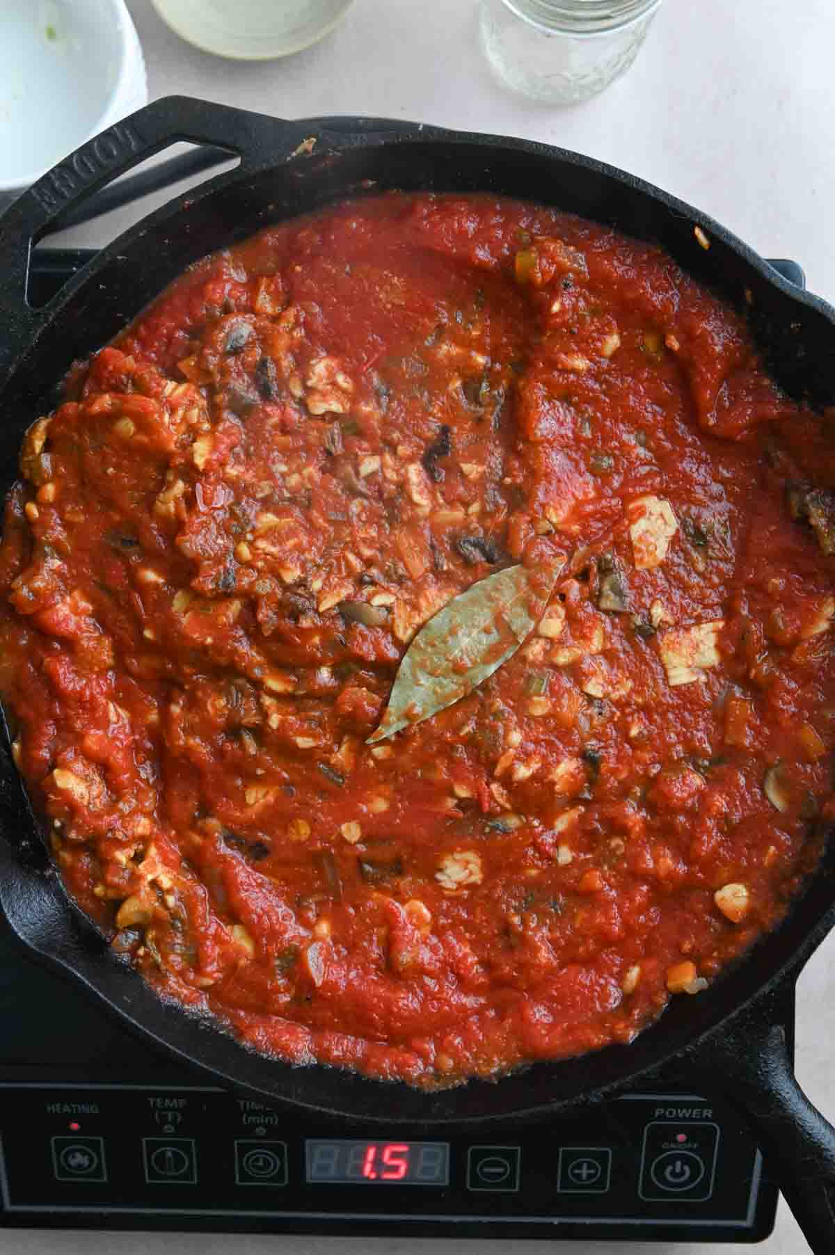 Tomato sauce topped with bay leaf in a cast iron skillet.