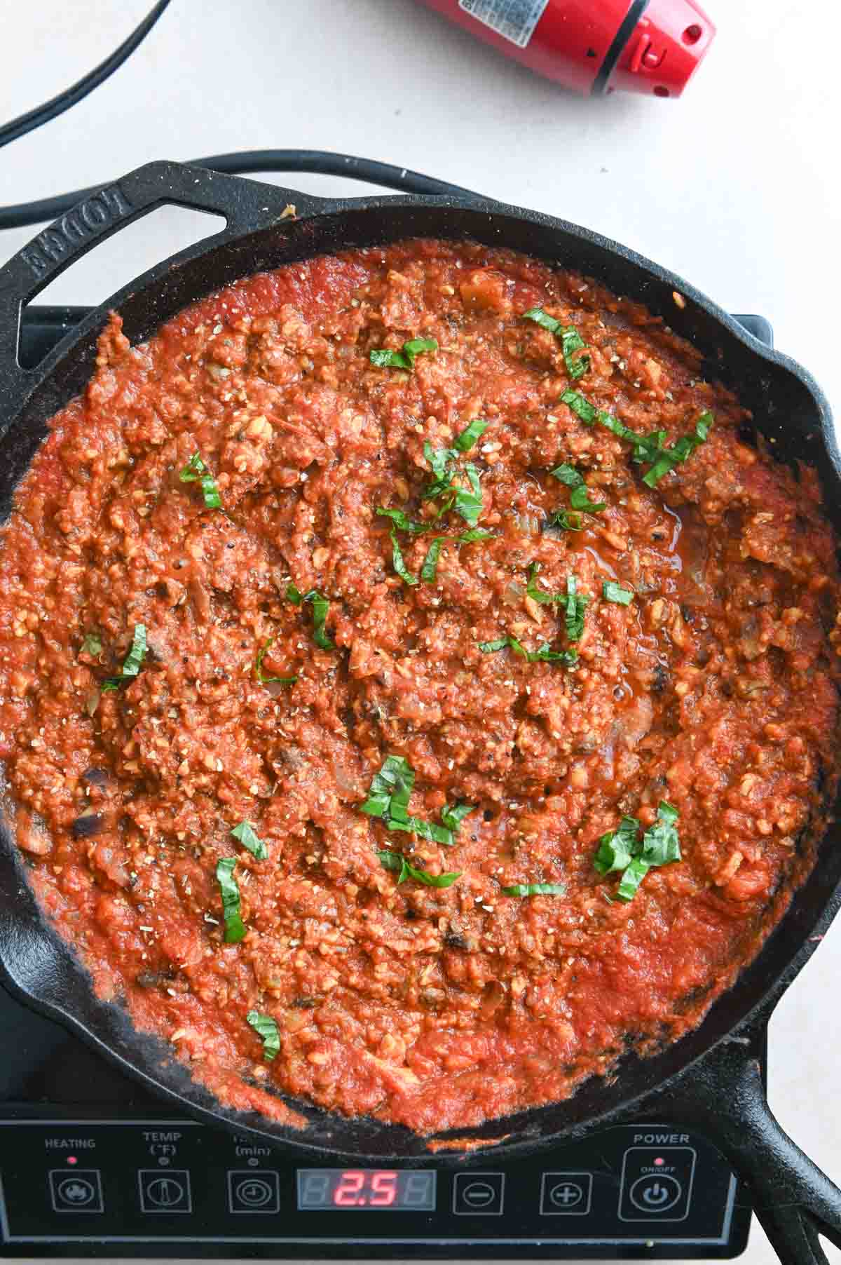 Tempeh bolognese sauce in a cast iron skillet topped with sliced basil.