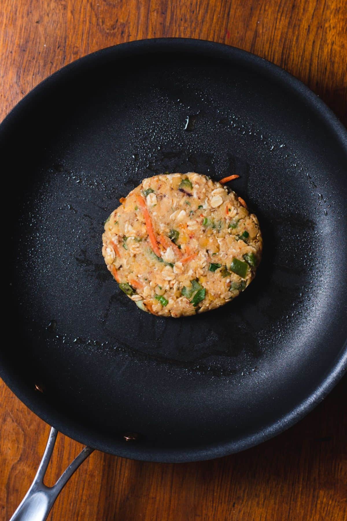 One red lentil patty being cooked in a black skillet.