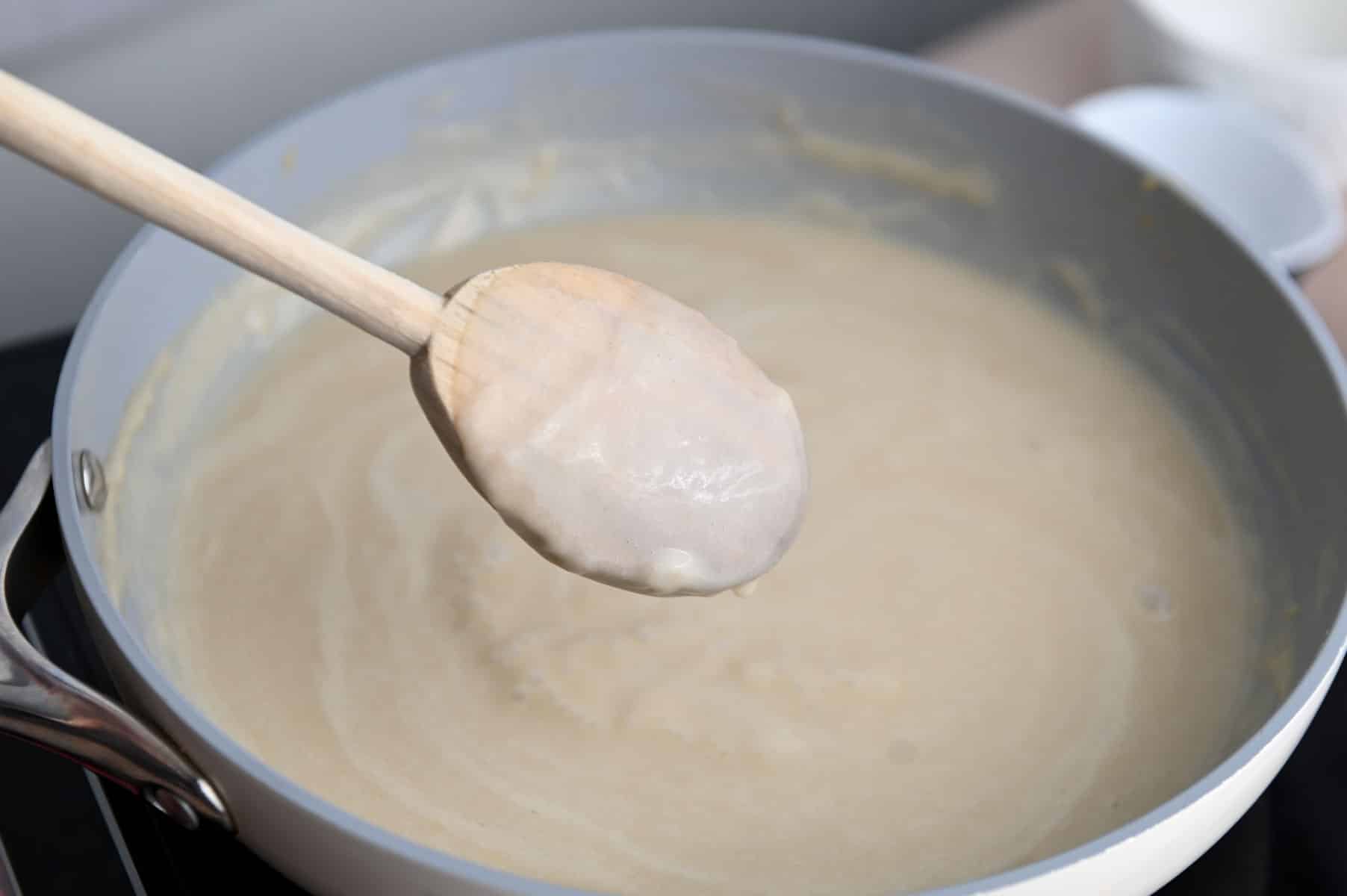 Wooden spoon lifted to show béchamel sauce on the spoon.