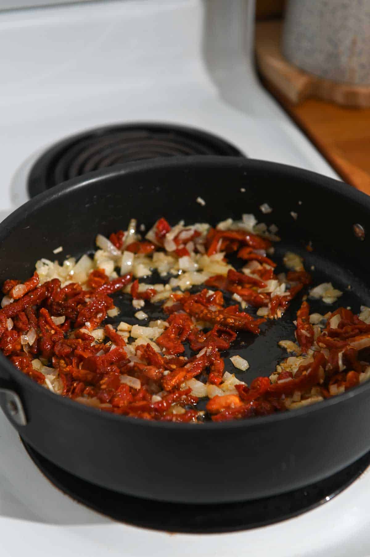 Sundried tomato and onion sautéing in a black skillet.