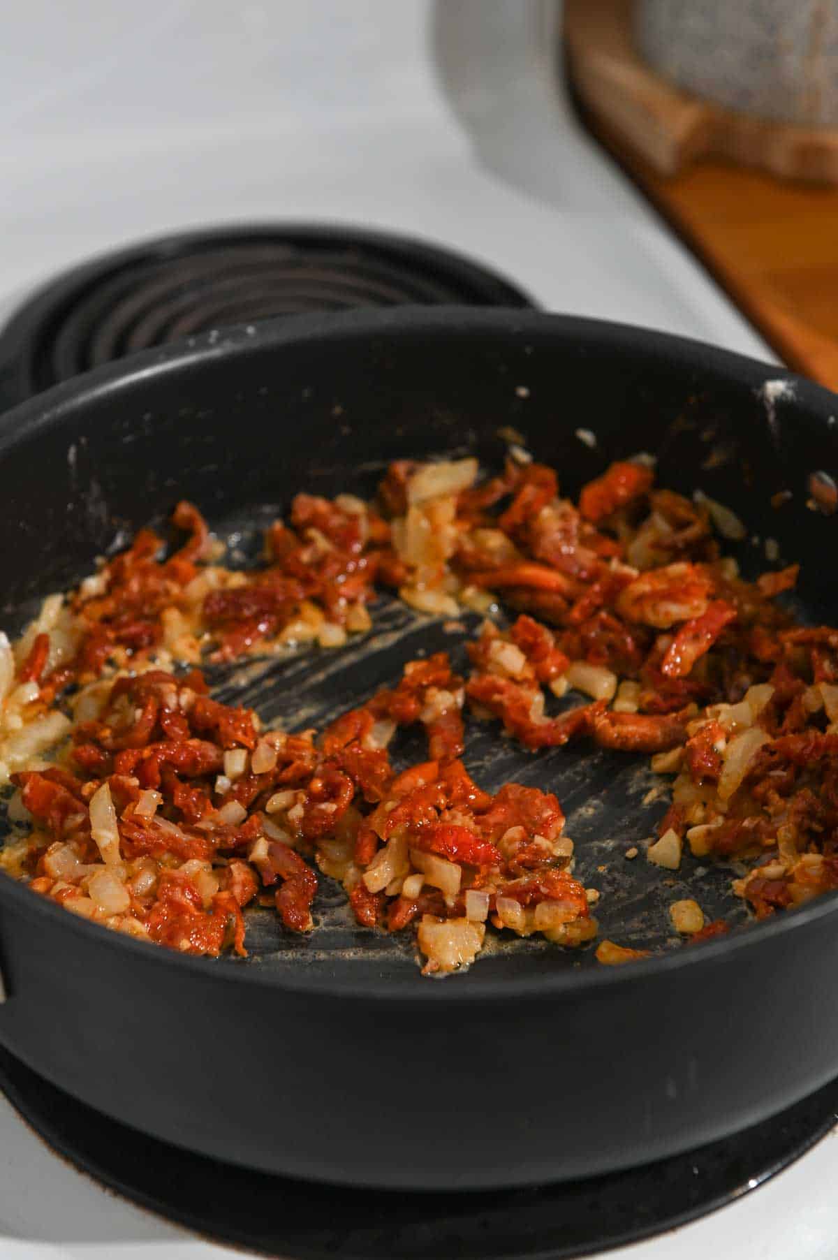 Flour, sundried tomatoes, and onions sautéing in a black skillet.