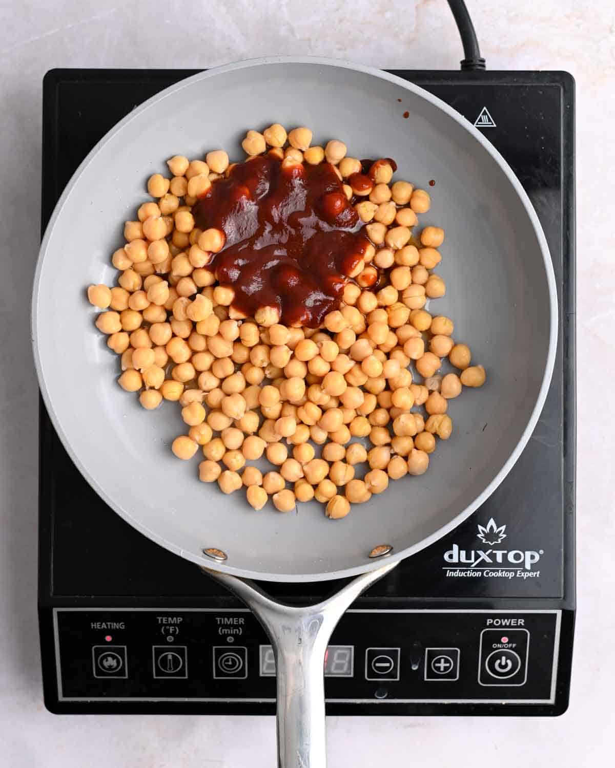 Chickpeas and BBQ sauce in a skillet on an induction stove.