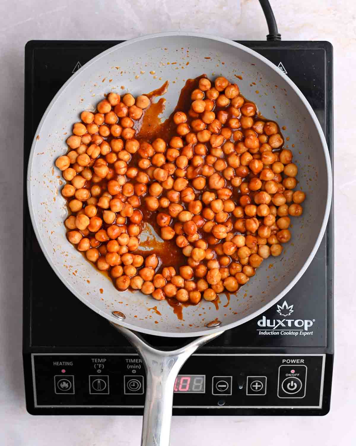Chickpeas coated in BBQ sauce in a skillet on an induction stove.