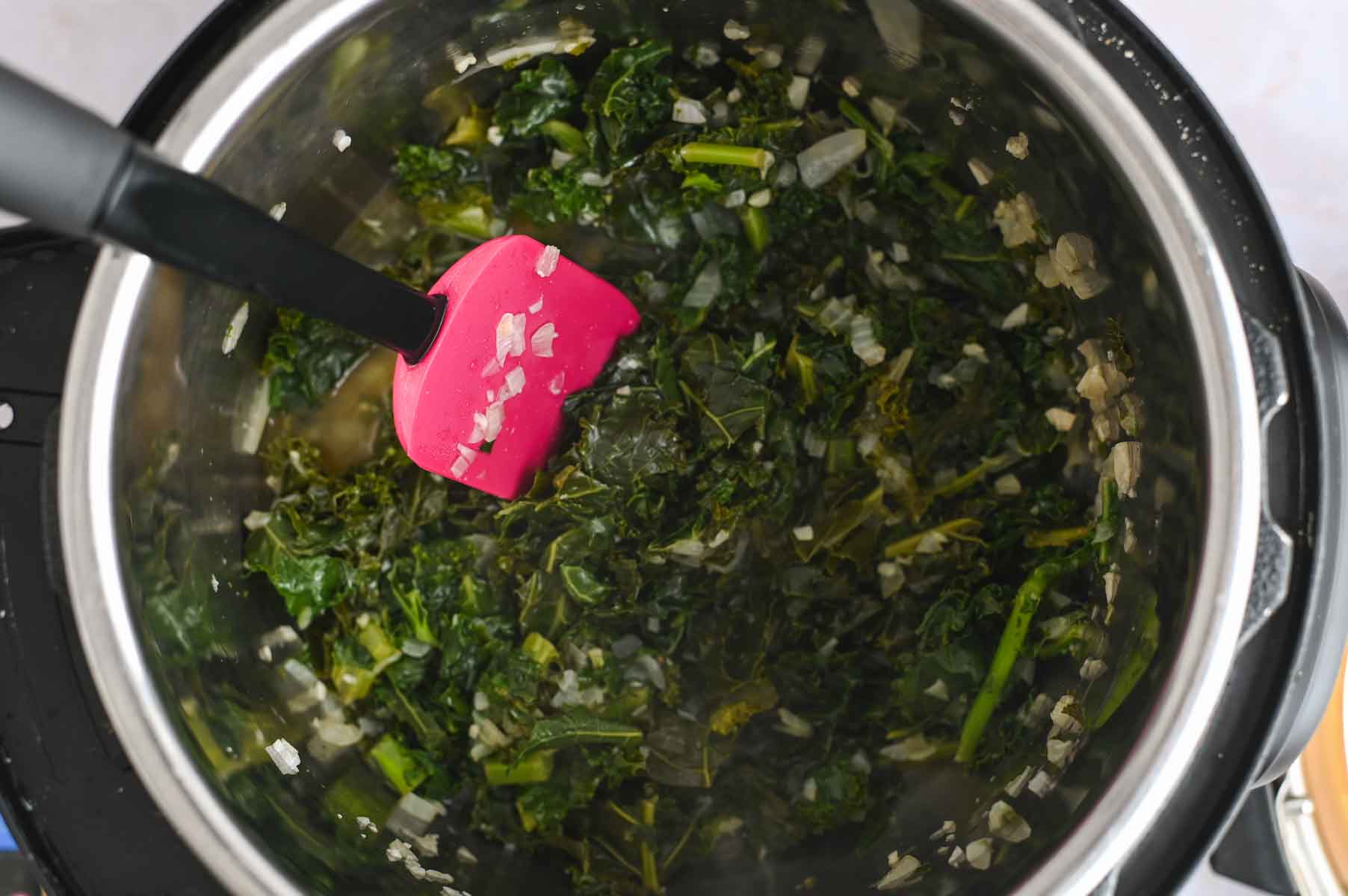 Stewed kale greens with a pink spatula in the Instant Pot.
