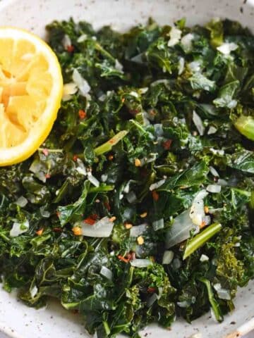White bowl filled with stewed kale and half of a lemon.
