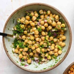 Overhead view of marinated chickpeas in a gray bowl with a black-handled utensil.