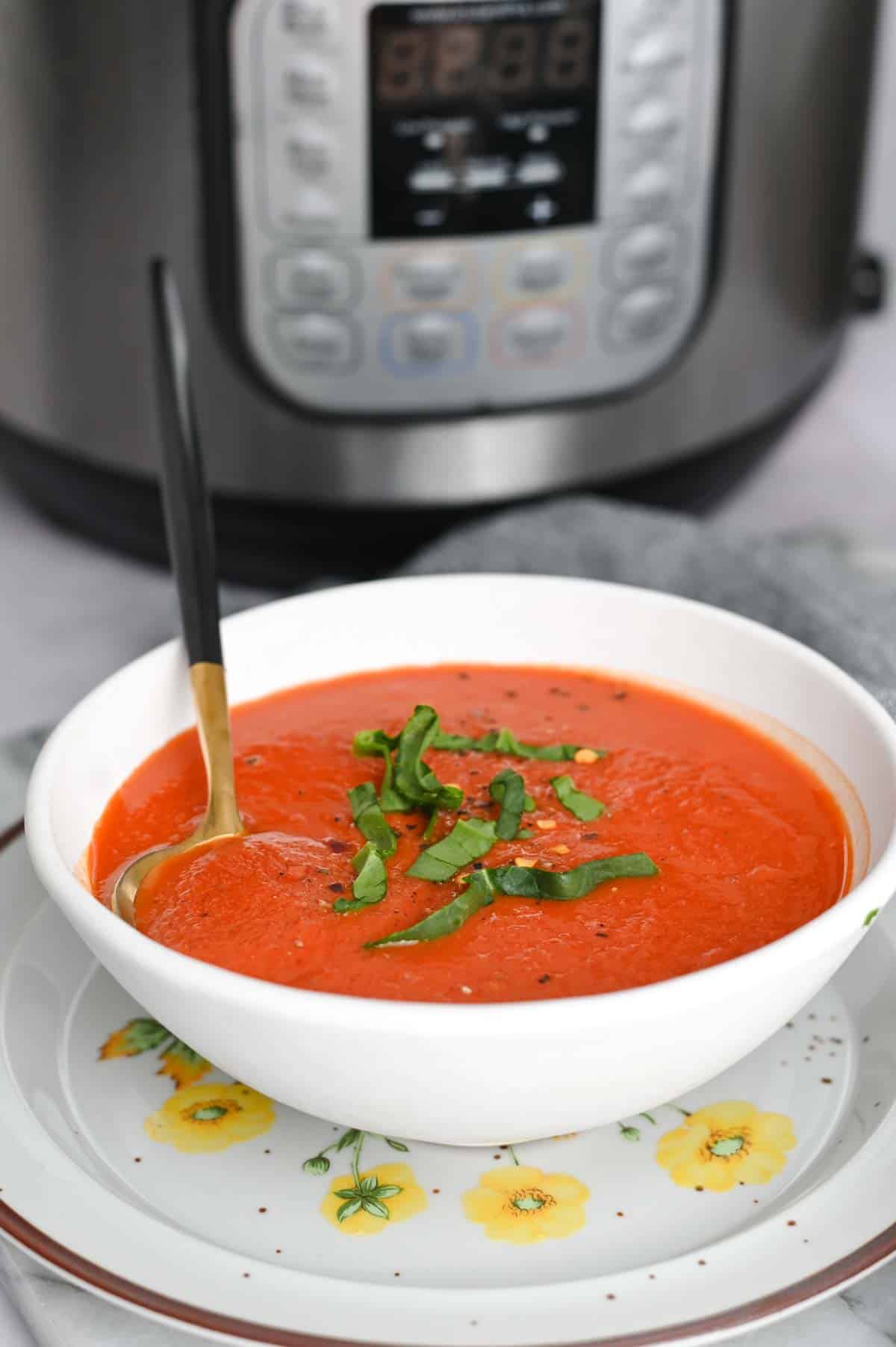 Side view of white bowl with red tomato soup in front of an Instant Pot.