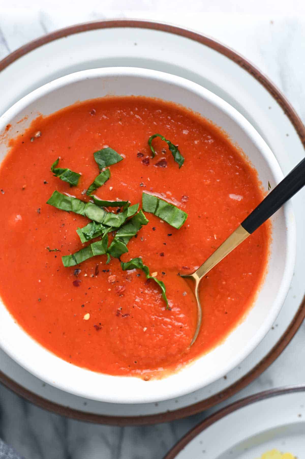 Close up of white bowl filled with vivid red tomato soup and sliced basil.