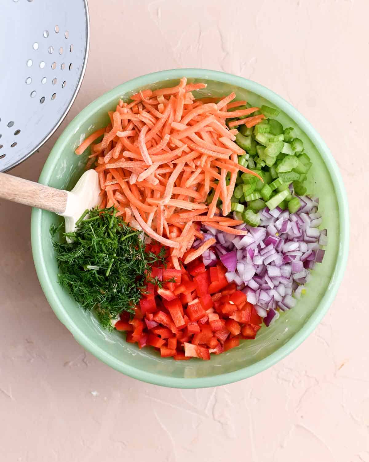 Green bowl filled with carrots, celery, onion, red pepper, and dill.
