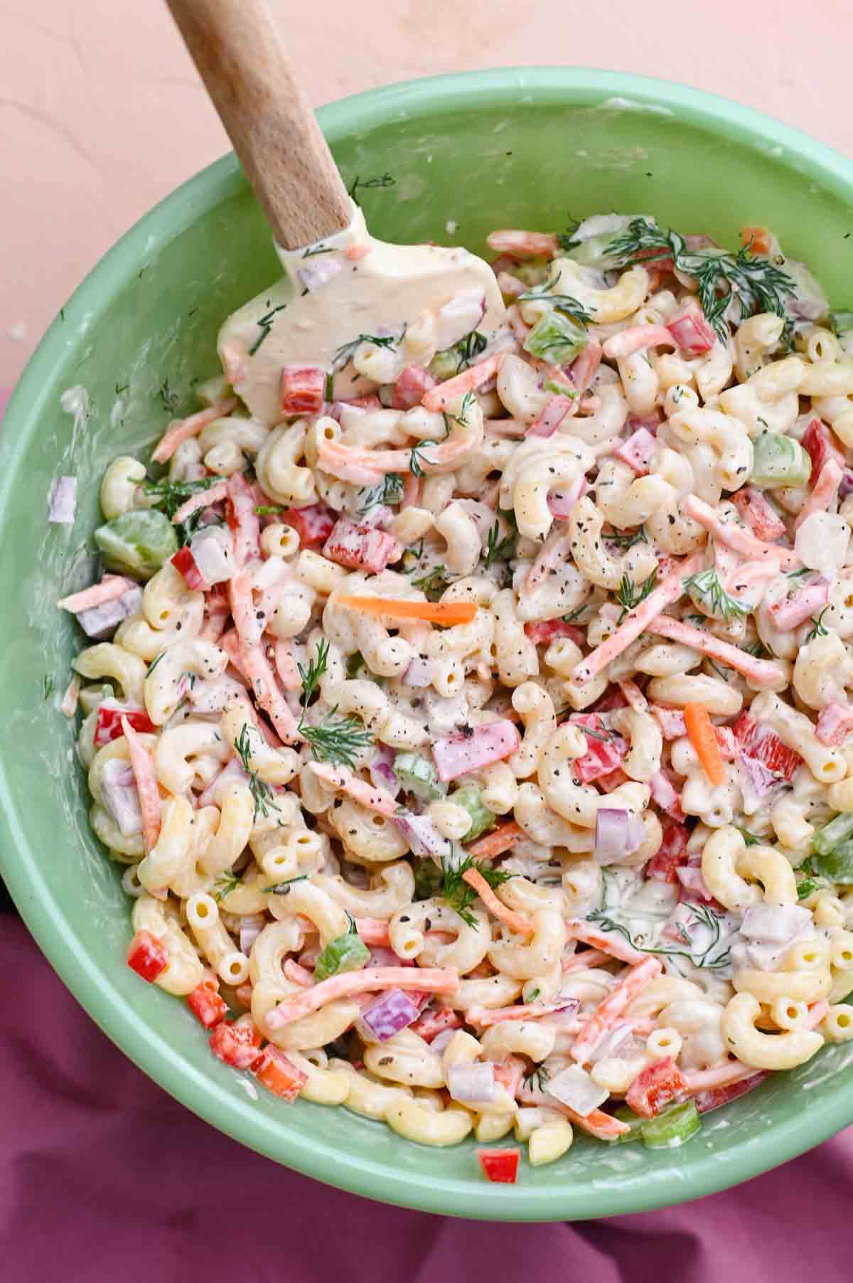 Green bowl filled with macaroni salad and a wood-handled spatula.