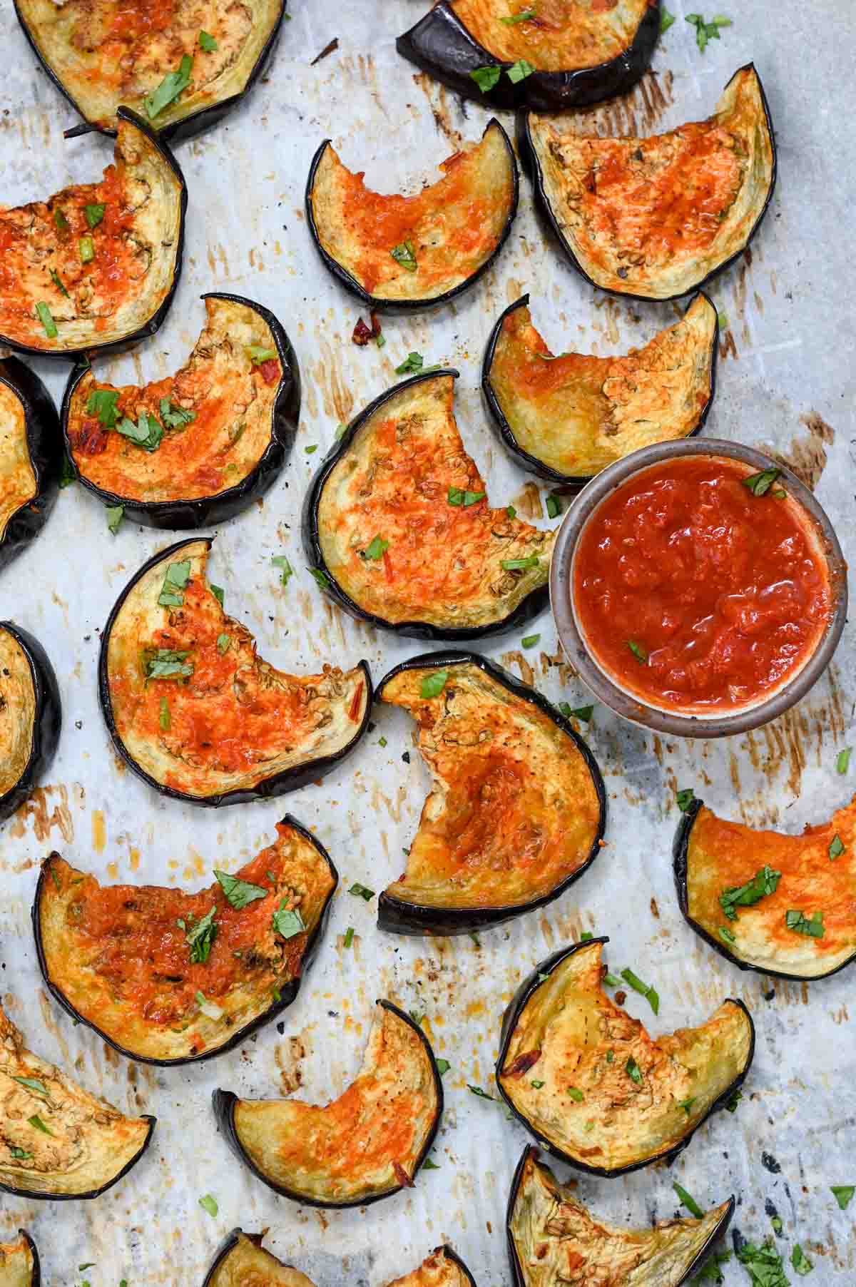 Slices of roasted eggplant on parchment paper next to a small bowl of harissa.