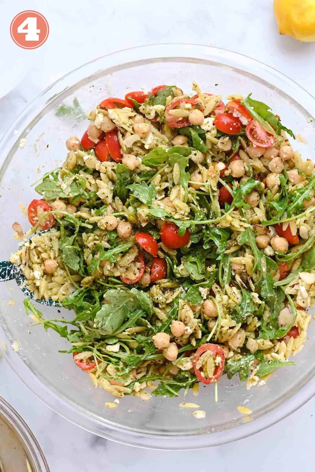 Close up of orzo salad with cherry tomatoes and arugula in a glass bowl.