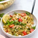 White bowl filled with pesto orzo salad in front of a glass bowl with more salad in it.