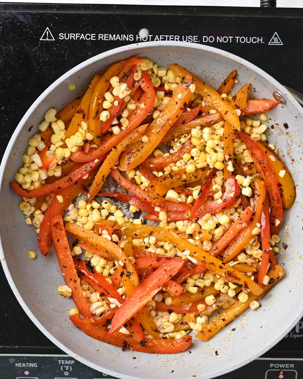 Corn, garlic, and peppers in a gray skillet.