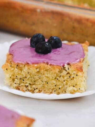 Side view of yellow crumb cake topped with blueberry glaze and three blueberries.