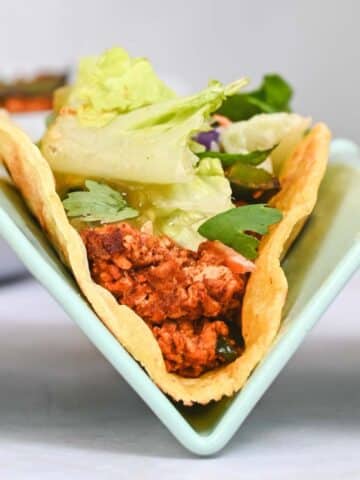 Close up of a tofu taco topped with lettuce in a blue taco holder.