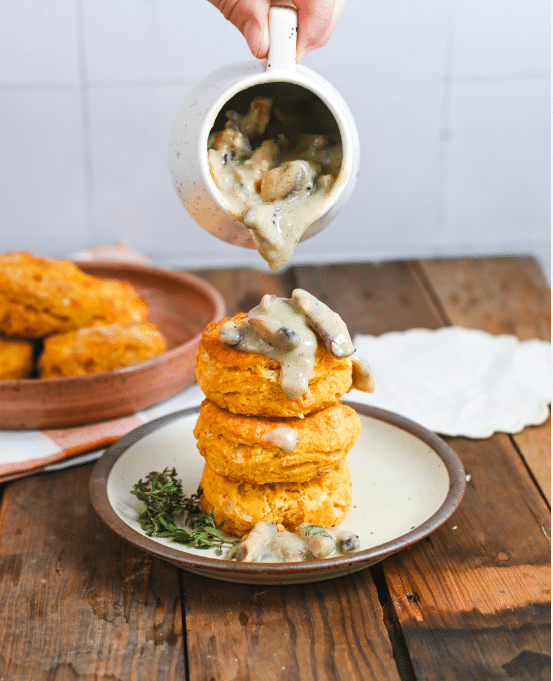 Three sweet potato biscuits stacked on top of each other while being drizzled with gravy.