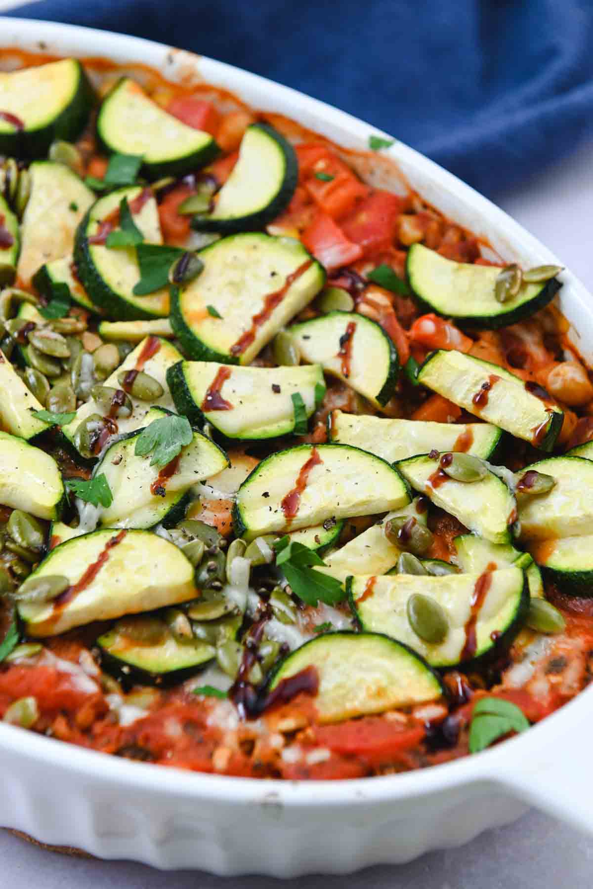 Close up of sliced zucchini on top of farro casserole in a white baking dish.