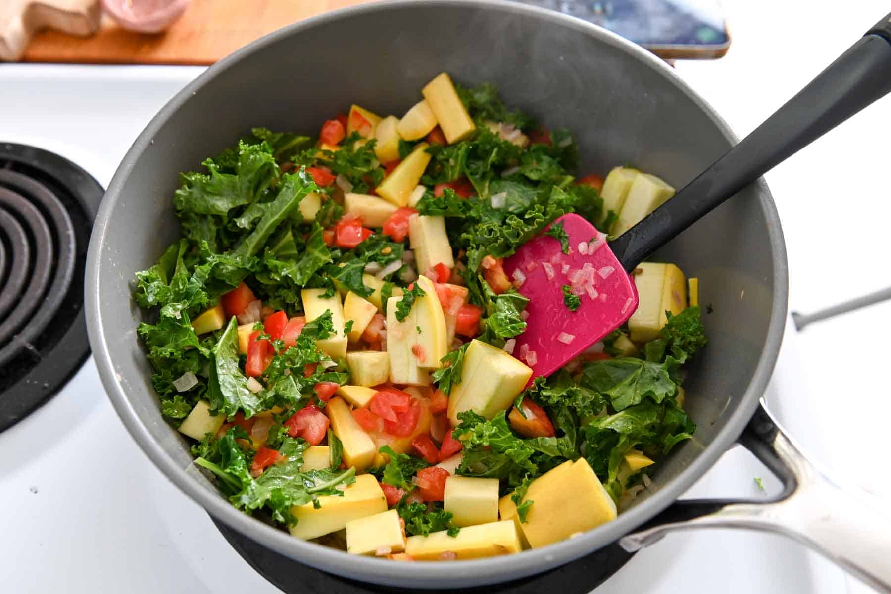 Kale, squash, tomatoes, and shallots in a gray pot.