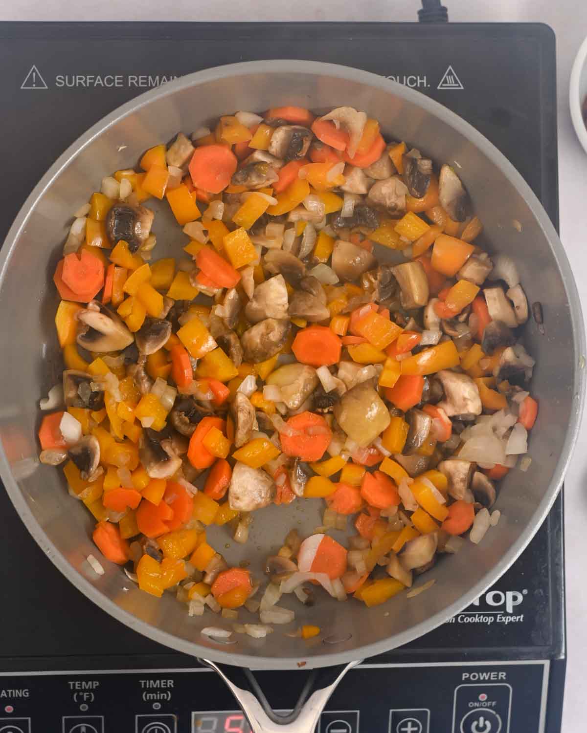 Carrots, mushrooms, onions, and peppers sauteing in a gray skillet.