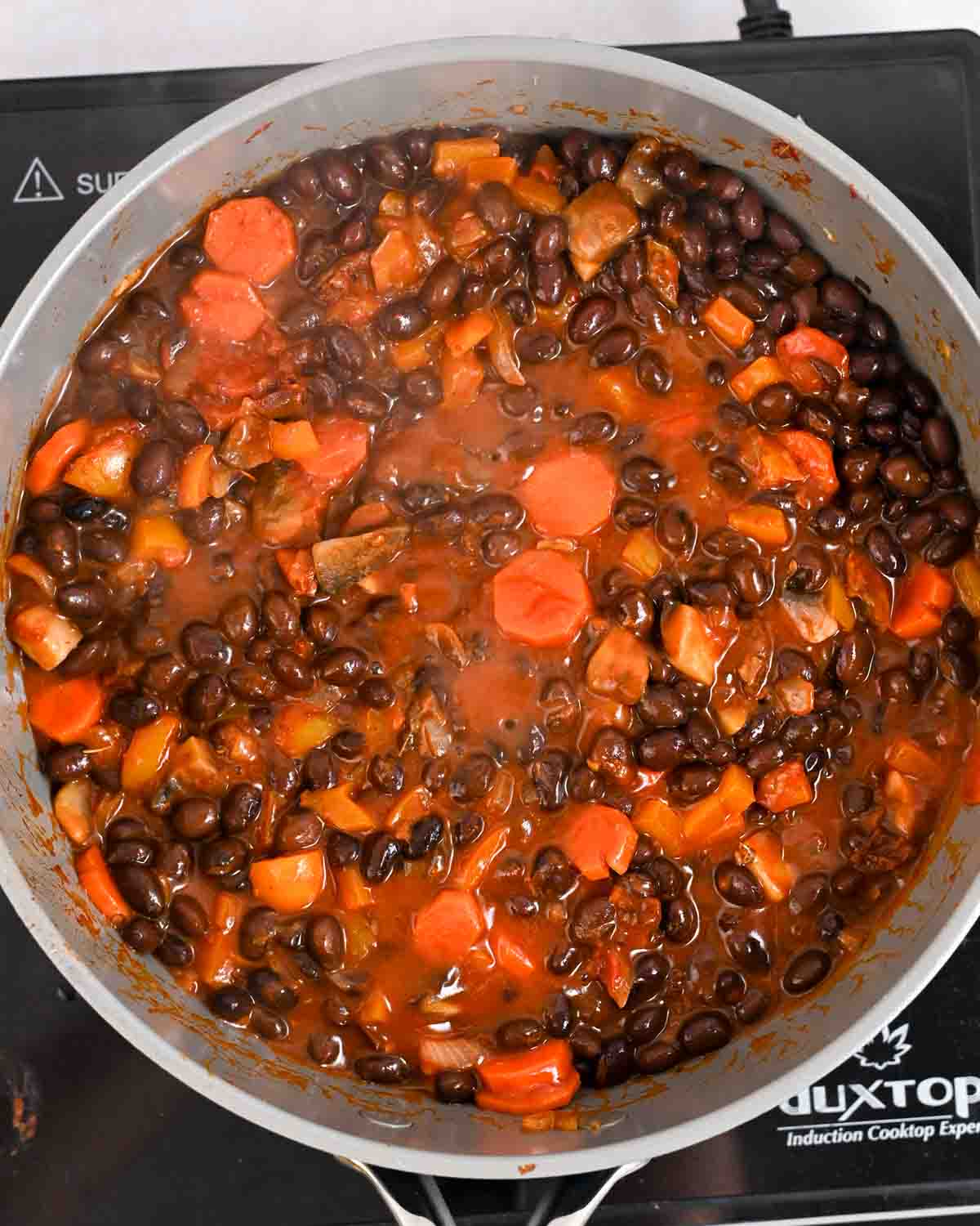 Close up of black beans and vegetables simmering in a gray pot.
