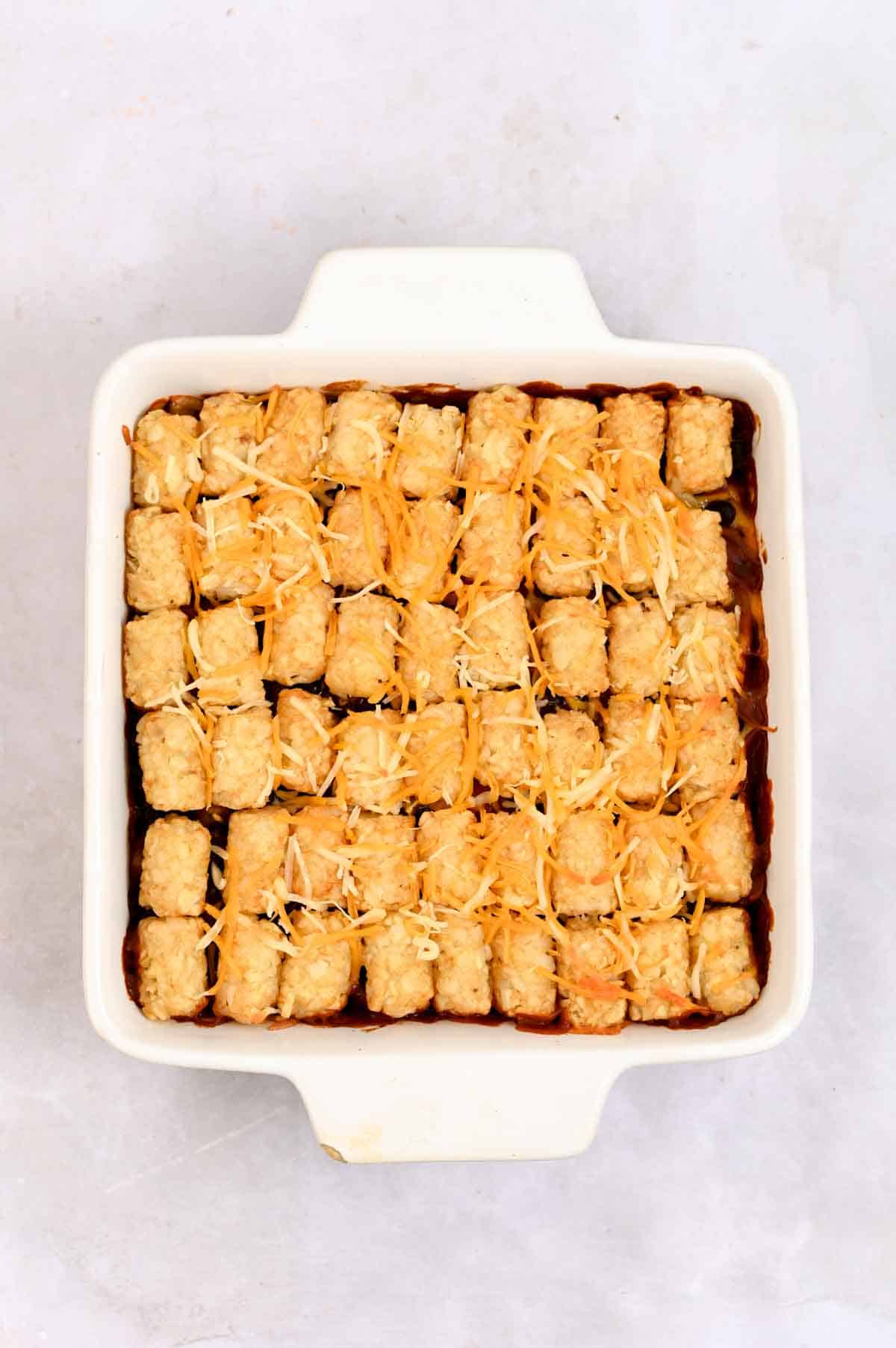 Golden tater tots with melted cheese on top lined up in a row in a white-handled baking dish.