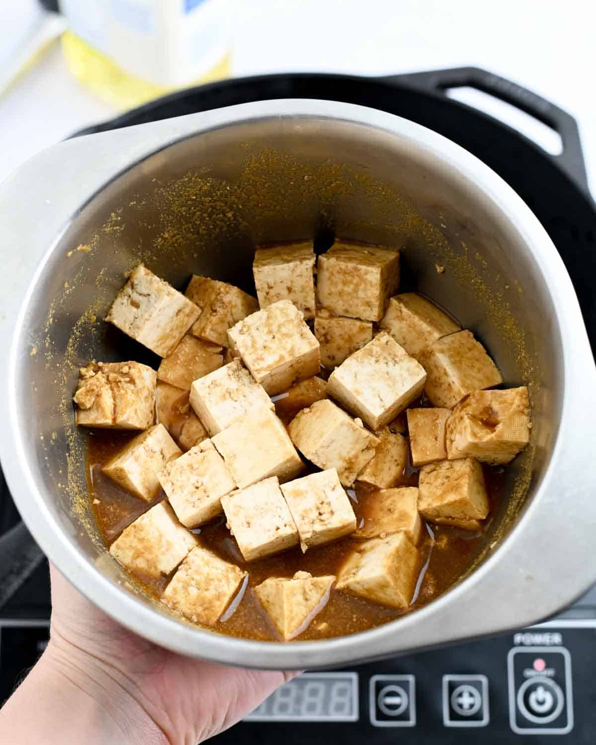 Cubed tofu in a brown marinade in a metal bowl.