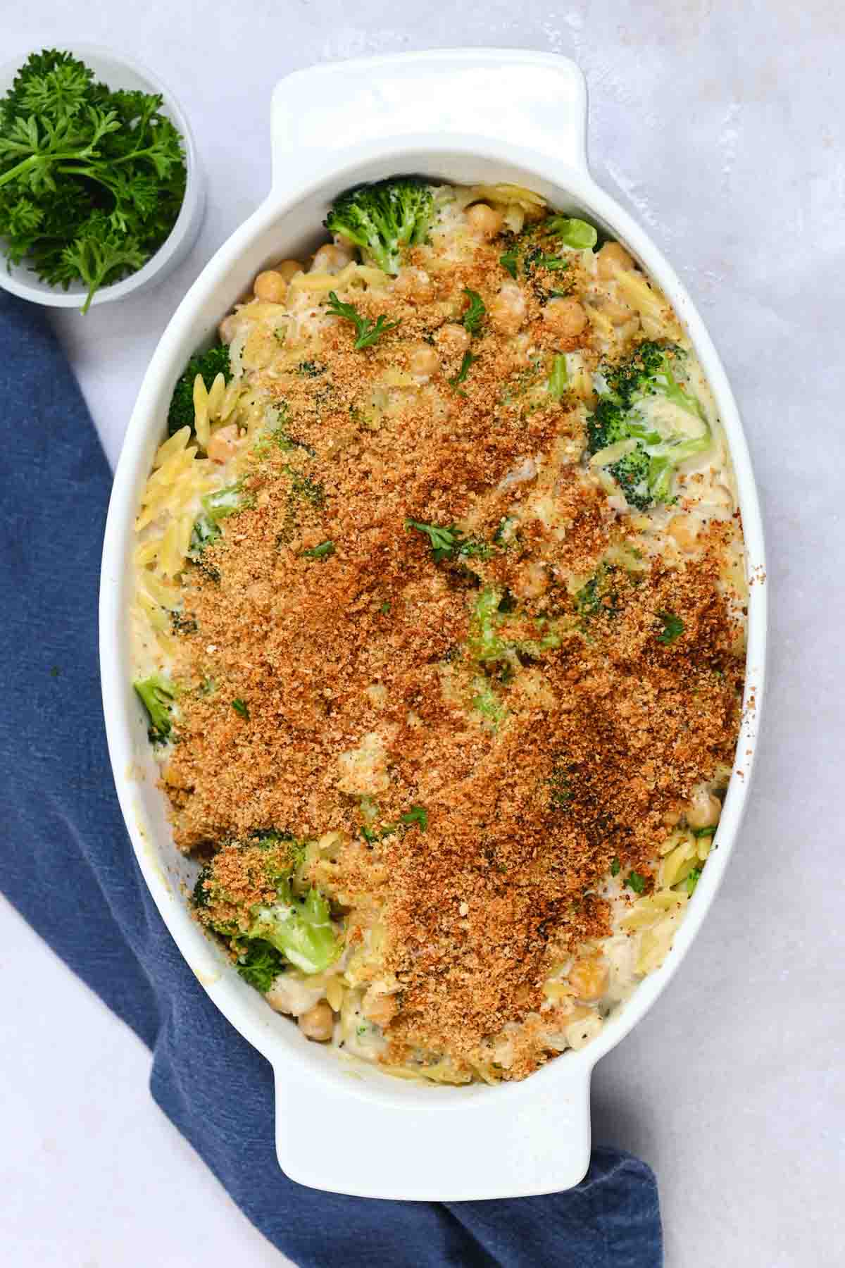 White oval casserole dish filled with orzo casserole topped with toasted breadcrumbs.