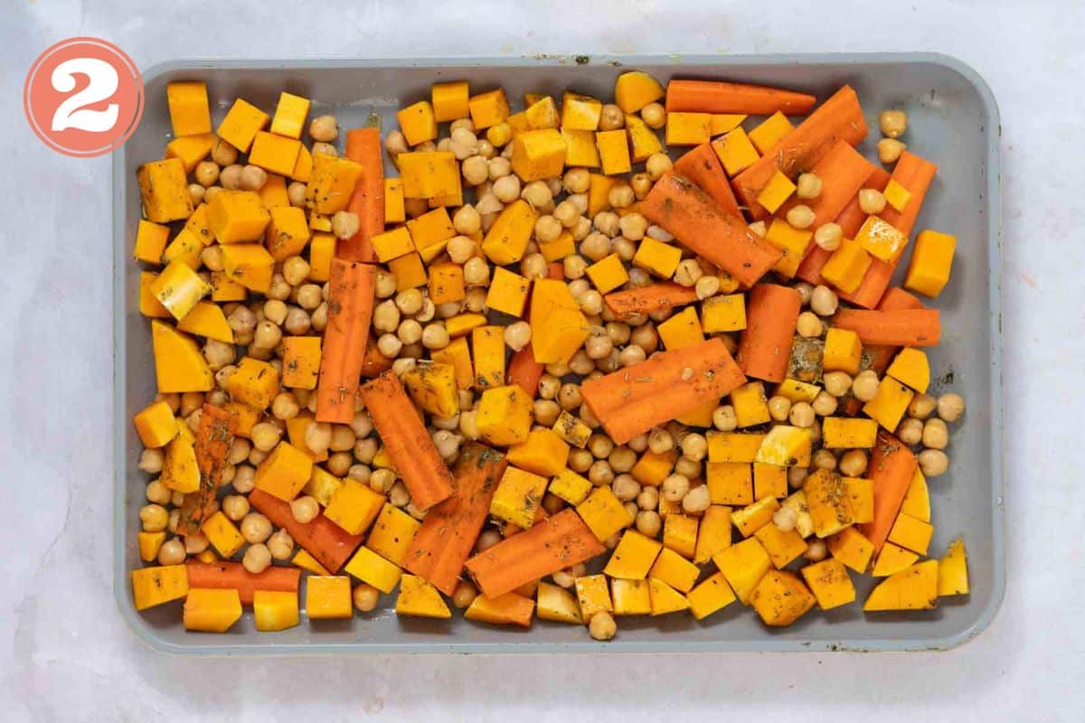 Cubed butternut squash, carrot wedges, and chickpeas on a sheet pan.