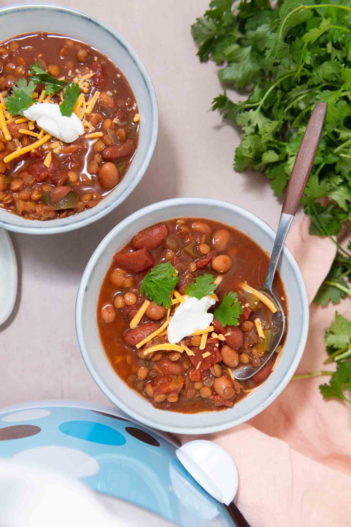Two bowls of lentil chili next to cilantro and a blue crockpot.