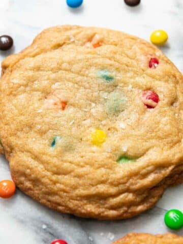 Close up of golden M&M cookie on a marble surface surrounded by mini M&Ms.