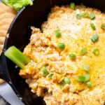 Close up of cheesy dip in a cast iron skillet with a slice of celery in it.