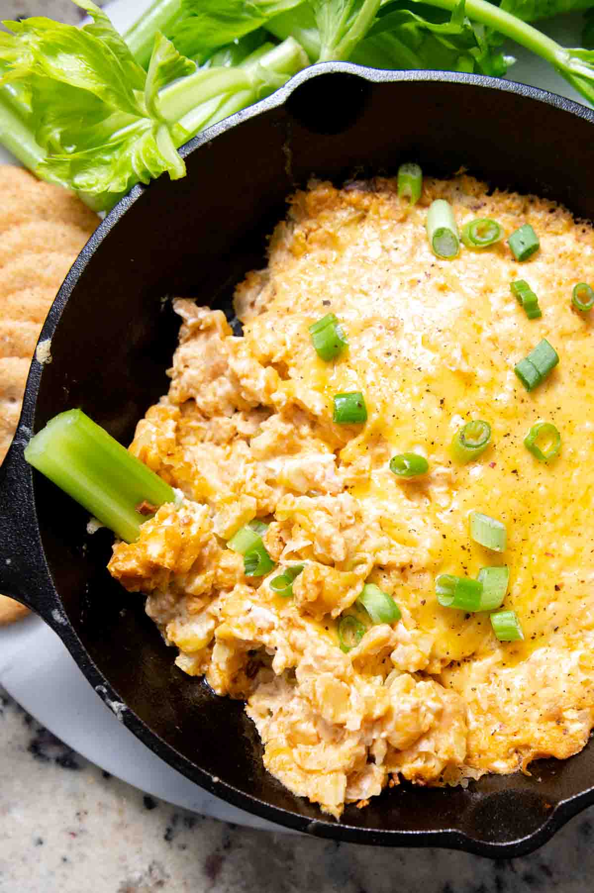 Close up of cheesy dip in a cast iron skillet with a slice of celery in it.