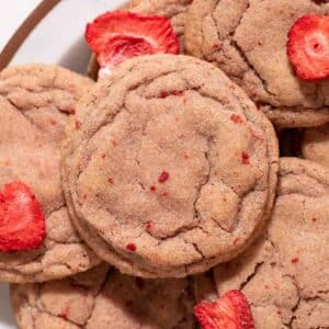 Pink strawberry cookie on a pile of cookies and freeze dried strawberries.