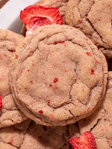 Pink strawberry cookie on a pile of cookies and freeze dried strawberries.