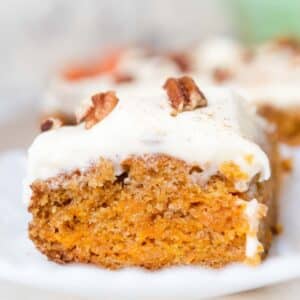 Close up of orange slice of carrot cake topped with frosting and pecans.