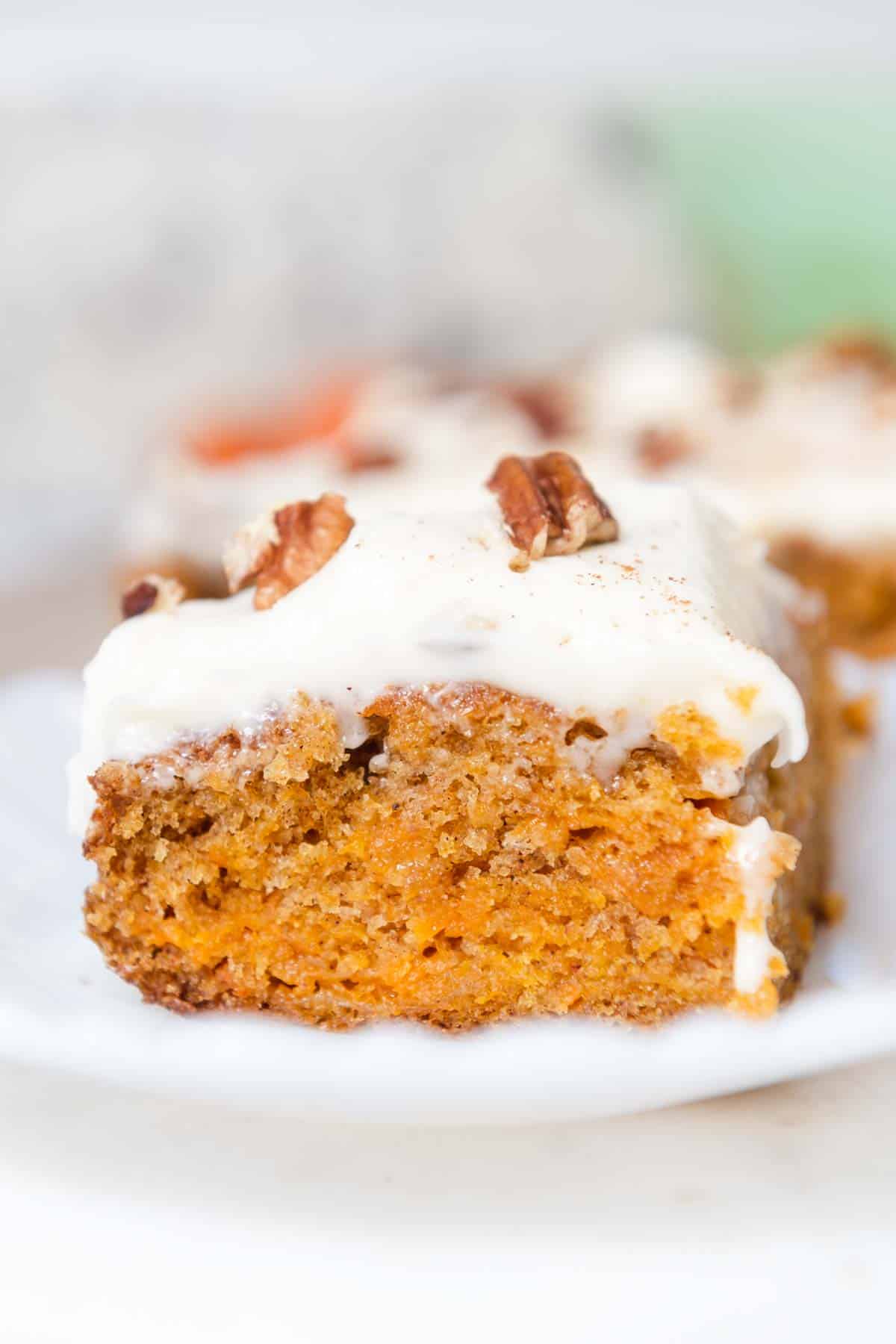 Close up of orange slice of carrot cake topped with frosting and pecans.