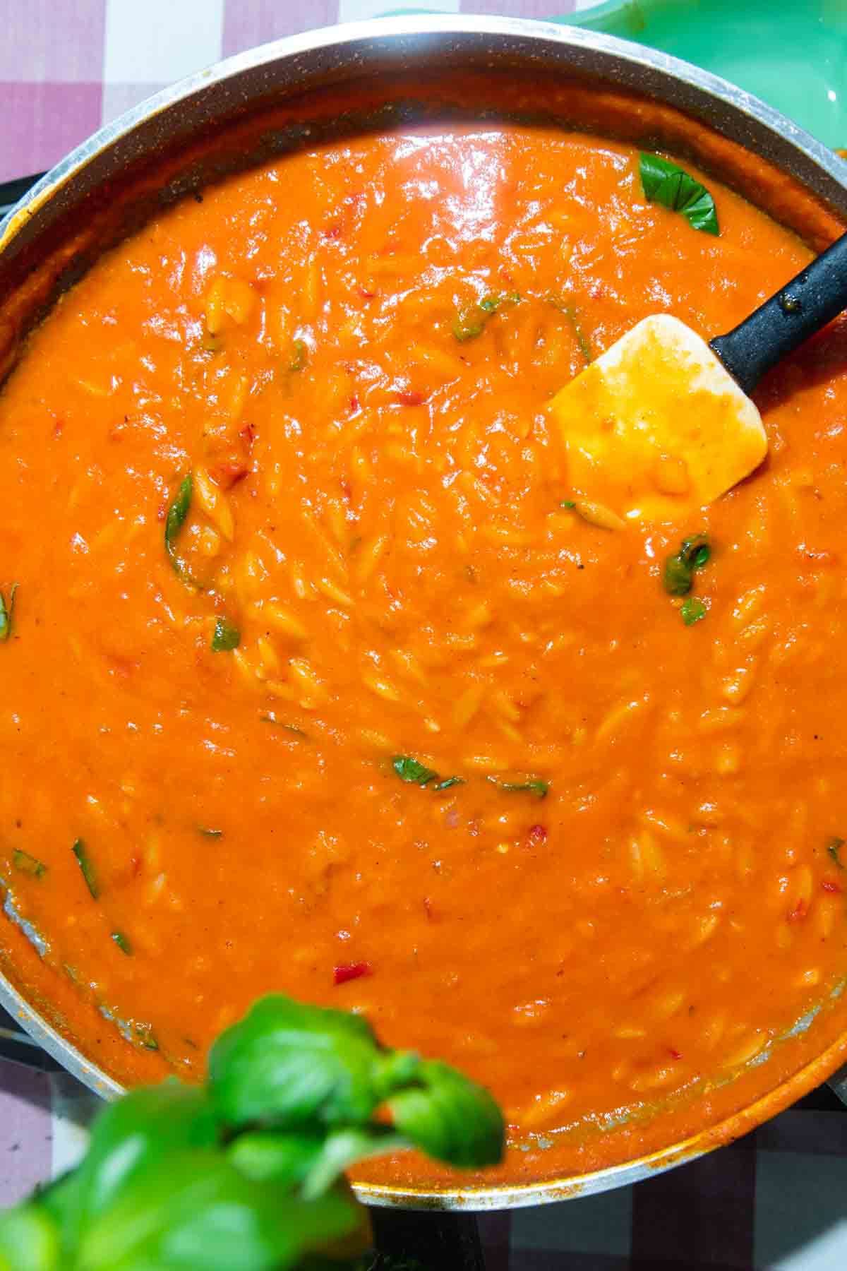Orzo in an orange sauce in a skillet with a white spatula.